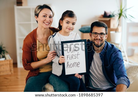 Happy family holding picture frame with 'our new home' inscription while moving into a new house.  