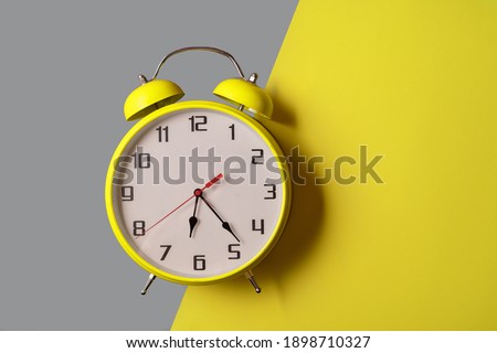 Illuminating color Retro style alarm clock on ultimate gray and yellow background, front view.