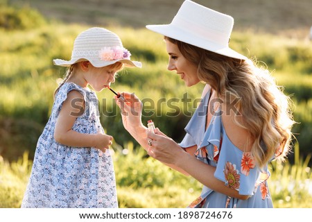 Young mother with daughter is having fun in the field on summer day. Family holiday in garden. mom doing little daughter makeup on nature. Mum, little daughter outdoors. Happy Mothers Day. Close up