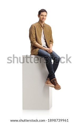 Casual young man sitting on a white column isolated on white background Royalty-Free Stock Photo #1898739961