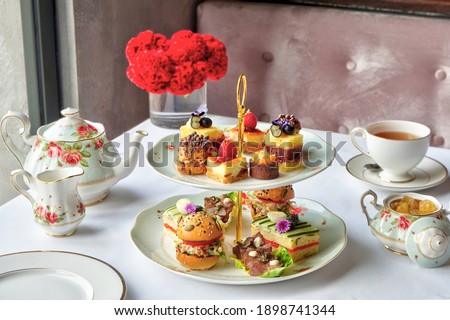 A set selection of finger sandwiches, petit fours, sweet and savory pastries, scone with preserve and clotted cream, tea, or coffee. Tea Selection included. Royalty-Free Stock Photo #1898741344