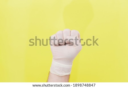 Fist of a doctor in a white medical glove on a yellow background. The medicine. Successful operation. The doctor is a hero. Covid 19. Place for an inscription. Advertising. Coronavirus.