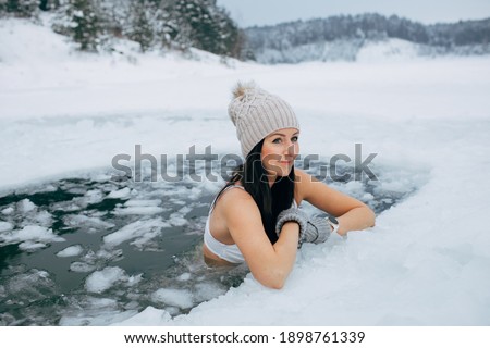 Winter swimming. Woman in frozen lake ice hole. Swimmers wellness in icy water. How to swim in cold water. Beautiful young female smiling. Gray hat and gloves swimming clothes. Nature lake in forest Royalty-Free Stock Photo #1898761339