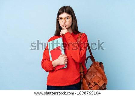 Young Ukrainian teenager student girl holding a salad over isolated blue background doing silence gesture