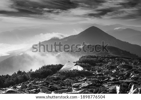 Morning dawn after rain with fog on the alpine stone wastelands of the Gorgan of the Carpathians of Eastern Europe. White tent glows in the rays of dawn over a misty valley
