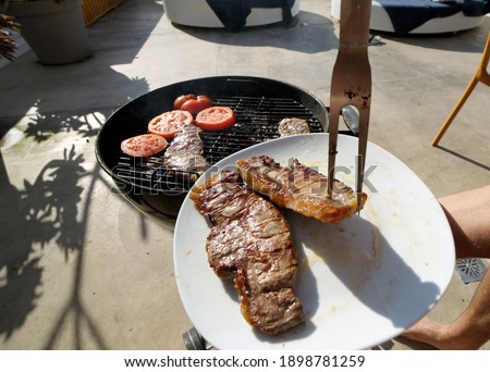 High angle view of two succulent steaks cooking on a barbecue over the hot coals on a green lawn outdoors