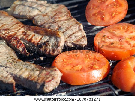 High angle view of two succulent steaks cooking on a barbecue over the hot coals on a green lawn outdoors