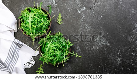 Fresh arugula salad leaves in two clay bowls on black rustic background with copy space for your design. Healthy diet food concept. Restaurant menu, cooking blog template. Minimalism style composition Royalty-Free Stock Photo #1898781385