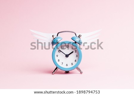 blue alarm clock with origami wing over pink pastel background. valentine romance day concept. greeting card template.