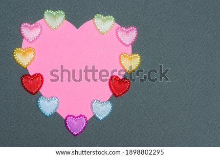 Pink valentine card in the shape of a heart and many small hearts on a gray background
