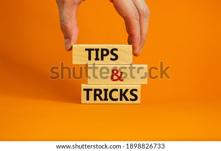 Tips and tricks symbol. Wooden blocks with words 'Tips and tricks'. Beautiful orange background. businessman hand. Business, tips and tricks concept. Copy space.