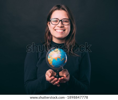 Excited young woman is holding a small Earth globe over black background.
