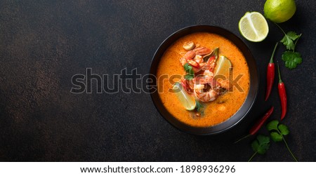 tom yum kung Spicy Thai soup with shrimp in a black bowl on a dark stone background, top view, copy space Royalty-Free Stock Photo #1898936296