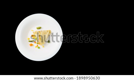 A thin pancake with a healthy filling on a white plate, over a black background with copy space. Corn, peas, asparagus and carrots are wrapped in a pancake. Healthy and balanced nutrition.