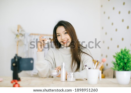 Beautiful asian woman blogger is showing how to make up and use cosmetics. In front of the camera to recording vlog video live streaming at home.Business online influencer on social media concept.