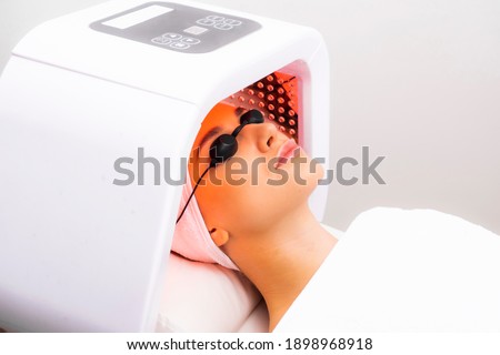 Express facial treatment with led therapy. Beautiful girl on a light therapy procedure. LED lamp with red light. Royalty-Free Stock Photo #1898968918