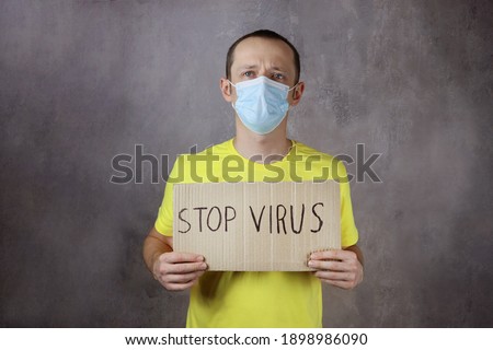 young man in a protective medical mask holds a Stop virus poster on a gray background