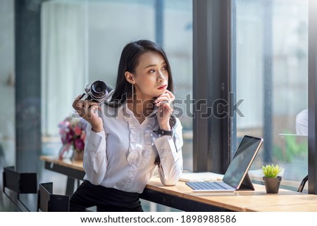 Young asian woman holding camera and tablet in a coffee shop.