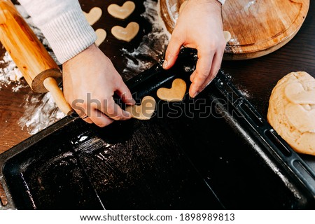 Cookies in shape of heart for the Saint Valentine's Day. Man is baking heart shape cookies for Saint Valentine's Day. Dough, flour, baking pan, round wooden cutting board and rolling pin on the table.