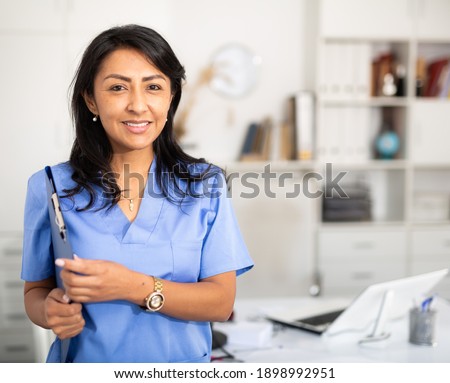 Closeup portrait of smiling hispanic woman health worker wearing blue uniform standing in medical office