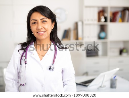 Latina woman doctor wear white medical uniform and stethoscope look at camera posing in private clinic Royalty-Free Stock Photo #1899008320