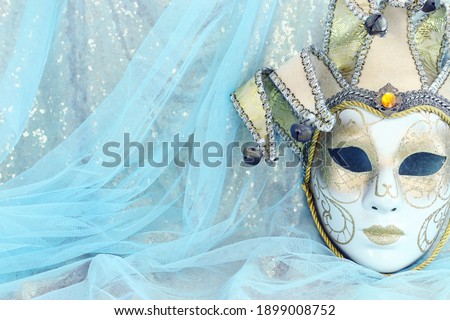 Photo of elegant and delicate Venetian mask over pastel blue and gold chiffon background