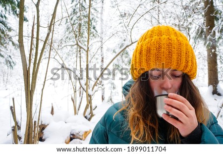 beautiful girl in the winter forest drinking a hot drink from the lid of a thermos close-up, tourism concept