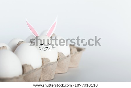 Creative concept photography. White eggs with hare ears and face in an eco-friendly paper tray, box . Happy Easter holiday concept. Minimalism