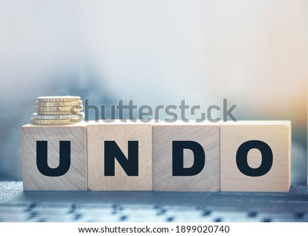 Undo word on wooden cubes with letters, and stack of coins. Technical issue computer program concept. Lifestyle and state of mind concept. Royalty-Free Stock Photo #1899020740