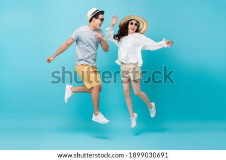 Smiling energetic Asian couple tourists in summer beach casual clothes jumping isolated on light blue studio background