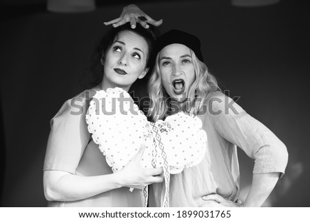Two girls in dresses indulge and laugh, in the background a black background. Two friends are having fun. Fun and joy concept. Portrait of two girls.