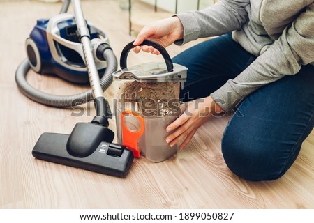 Woman opening dust filter out of vacuum cleaner at home on floor. Container full of dirt and cat's hair. Housework Royalty-Free Stock Photo #1899050827