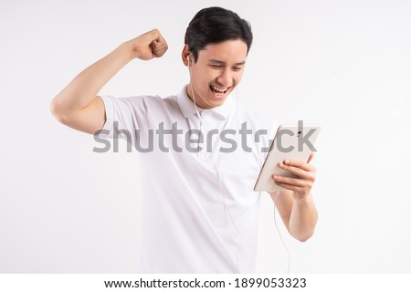 Image of happy young man standing on isolated white wall background. Look aside using the tablet as a winner gesture.
