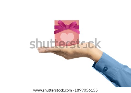 Human hand showing pink gift box with red ribbon and heart isolated over white background
