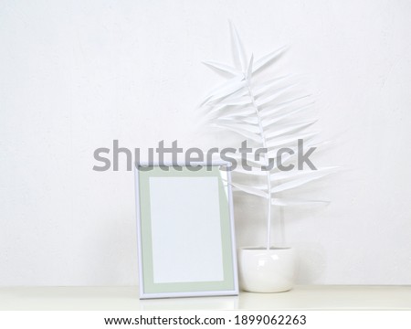 Mock up template for overlaying pictures, illustrations and patterns. Interior composition: photo frame and white  vase with white paper palm branch. Stylish still life