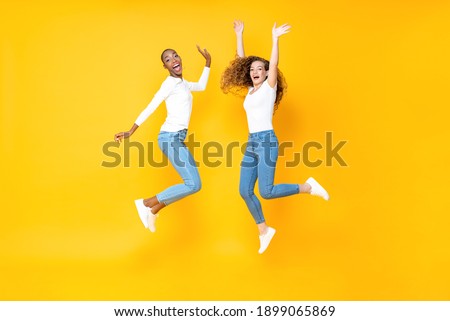 Two interracial woman friends jumping freely in isolated studio yellow color background