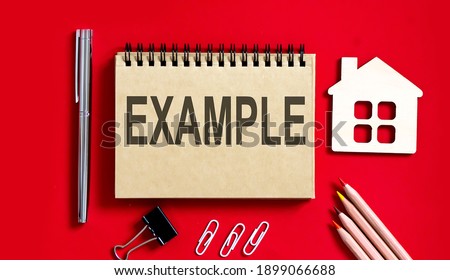 EXAMPLE text written on notebook with pencils and office tools and model wooden house