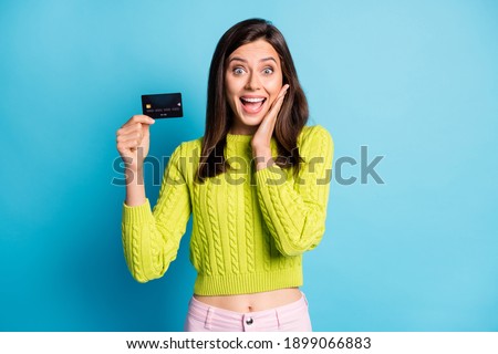 Photo of young attractive woman amazed surprised hold bank card hand touch cheeks isolated over blue color background