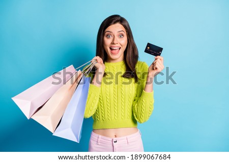 Photo portrait of excited girl holding shopping bags credit card isolated on pastel blue colored background