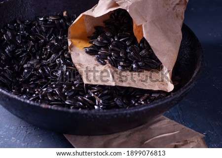 sunflower seeds in a paper craft bag and in a black charred cast iron frying pan with a handle on a gray concrete table in a dark key, rustic.