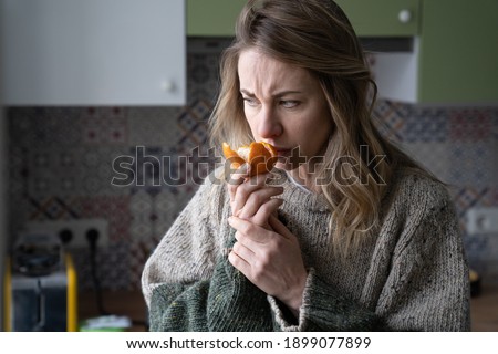 Sick woman trying to sense smell of fresh tangerine orange, has symptoms of Covid-19, corona virus infection - loss of smell and taste, standing at home. One of the main signs of the disease. Royalty-Free Stock Photo #1899077899