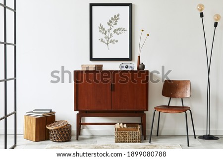 Modern retro concept of living room interior with design teak commode, black mock up poster frame, clock, chair, decoration, wooden cube, book, lamp, white wall and personal accessories. Template.