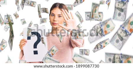Beautiful caucasian woman with blonde hair holding question mark with open hand doing stop sign with serious and confident expression, defense gesture