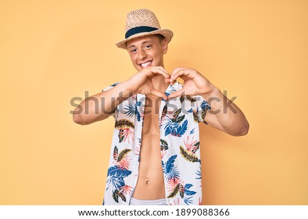 Young hispanic boy wearing summer hat smiling in love doing heart symbol shape with hands. romantic concept. 