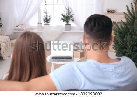 Couple using video chat on laptop in room decorated for Christmas