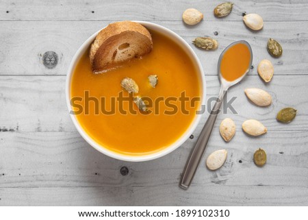 Pumpkin soup with bread on a light wooden background with spoon and seeds