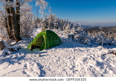Amazing landscape on the cold winter day. Sunset. On the lawn green touristic tent stands with wide path to it. Beautiful snowy forest with pine trees in mountains. Wallpaper background.