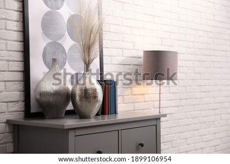 Grey chest of drawers with decor and books near white brick wall. Interior design
