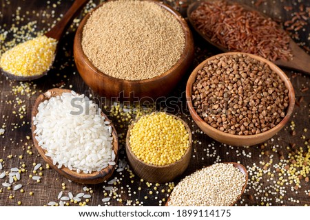 White and red rice, buckwheat, amaranth seeds, corn groats, quinoa and millet in bowls on a brown wooden table. Gluten-free cereals. Closeup Royalty-Free Stock Photo #1899114175