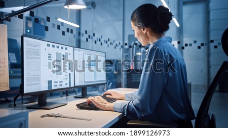 Factory Office: Portrait of Beautiful and Confident Female Industrial Engineer Working on Computer, on Screen Industrial Electronics Design Software. High Tech Facility with CNC Machinery Royalty-Free Stock Photo #1899126973